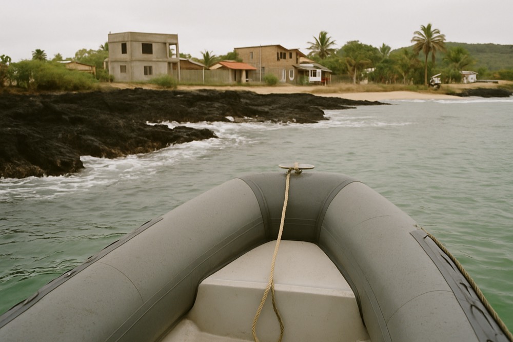 A small inflatable boat approaching a dark lava shoreline with gentle surf