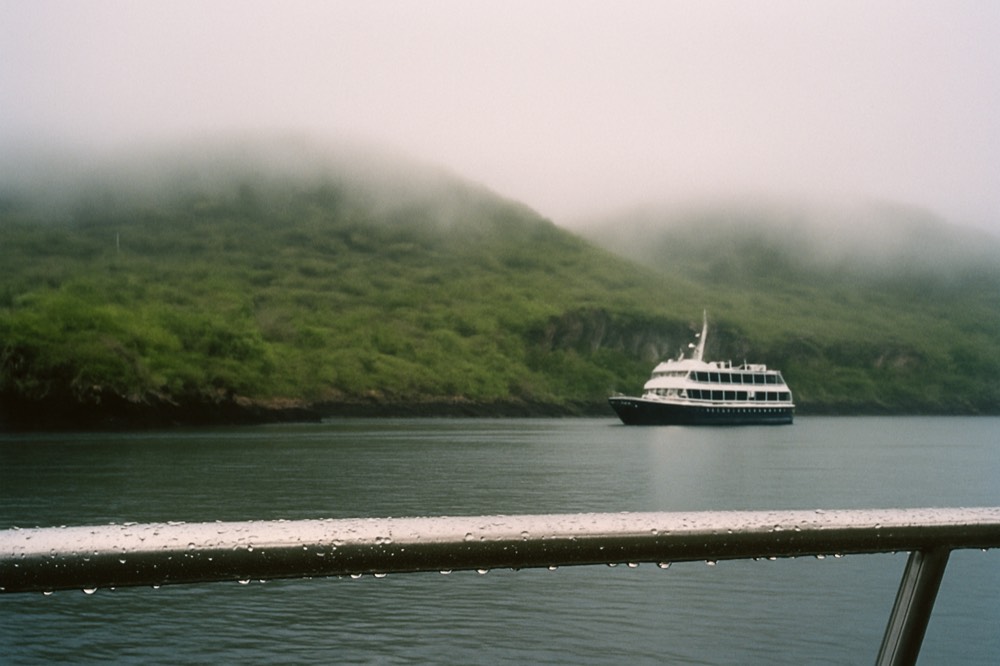 A small expedition boat anchored near a rocky Galapagos island with mist over the highlands