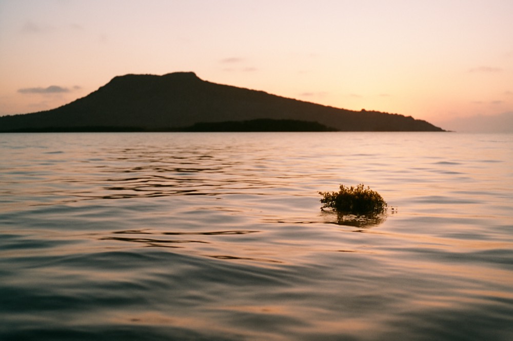 A glassy calm sea at sunrise with an island silhouette on the horizon