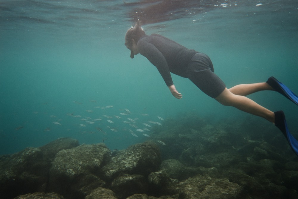 Snorkeller in a dark rash guard floating above a rocky reef in clear water