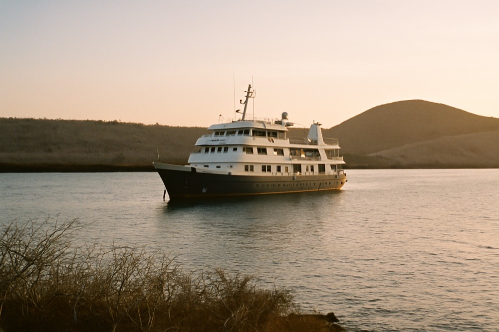 A mid-sized cruise vessel at anchor near a low, arid island at sunrise