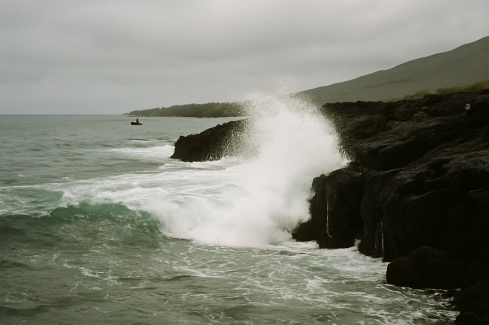 Ocean swell breaking against a rocky volcanic shoreline under low cloud