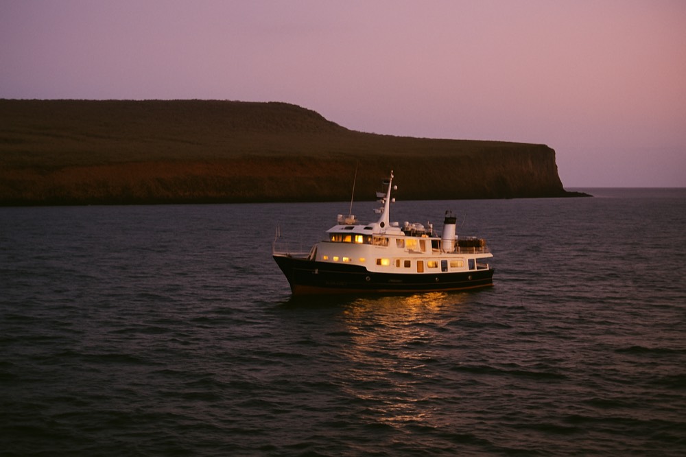 A small cruise ship anchored off a uninhabited volcanic island at dusk