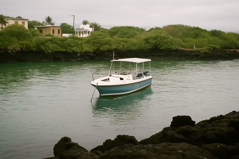 A small boat anchored in a sheltered cove with volcanic rocks and green shrubs along the shoreline
