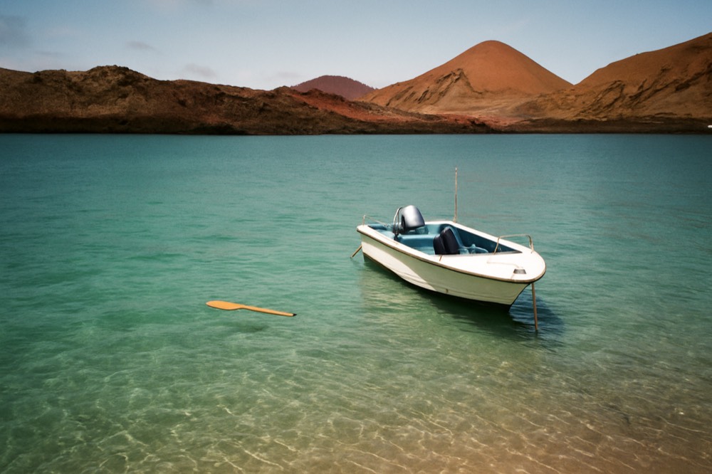Calm turquoise bay with a small boat and green volcanic hills behind