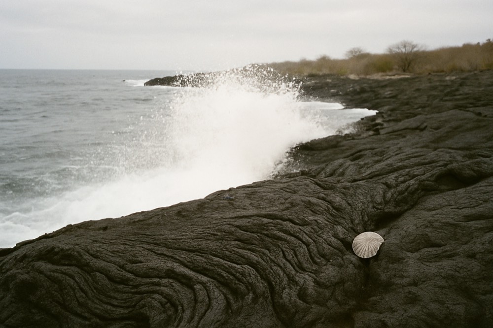 Waves breaking against a dark volcanic shore under an overcast sky