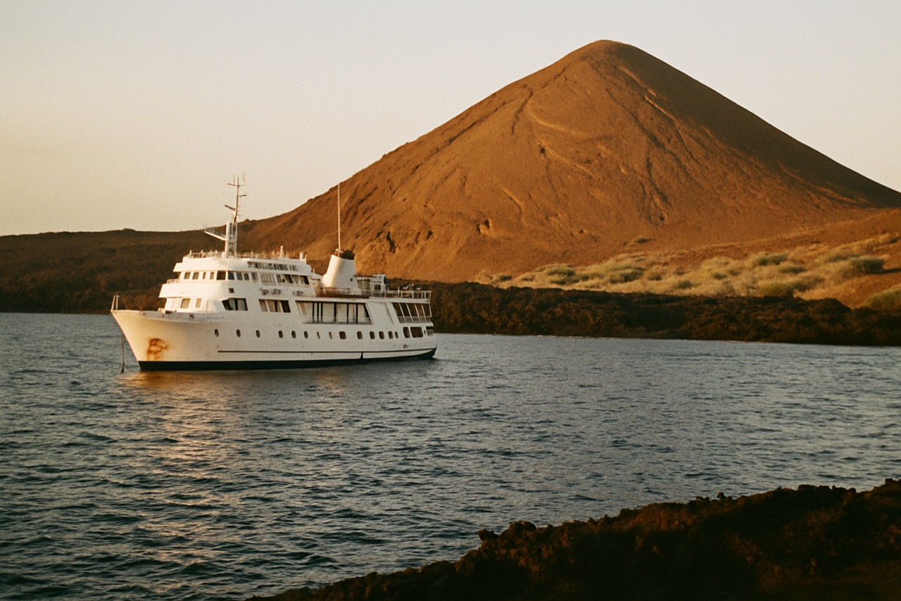 A small expedition ship anchored off a volcanic island in the Galapagos Islands, Ecuador, at golden hour